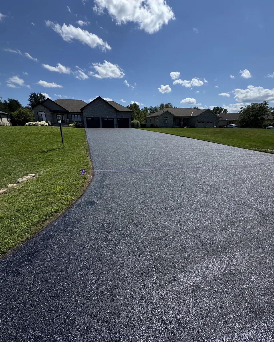Wide residential asphalt driveway fully coated with sealer.